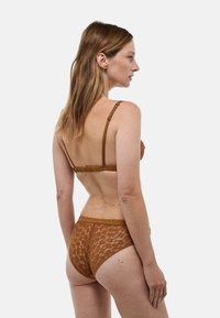 Soutien-gorge en dentelle marron et bas taille haute, ornés de motifs délicats, avec des bretelles réglables et une taille douce. Tissu texturé avec un aspect transparent.