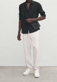 Zwarte button-up-shirt met opgerolde mouwen, gecombineerd met lichtbeige broeken en witte sneakers. Het shirt heeft een soepele textuur en een semi-formele uitstraling.