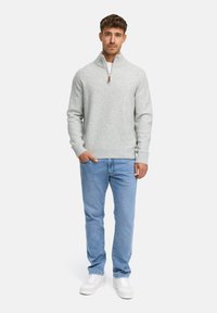 Ljust grått stickat tröja med hög krage och halvmatchande dragkedja, parat med ljusblå denimjeans och vita sneakers.