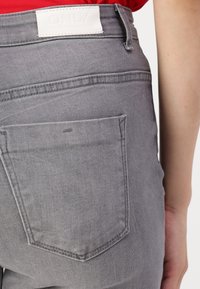 Jeans de mezclilla gris con un bolsillo trasero, que presentan una etiqueta de cuero blanco etiquetada "ONLY". La tela tiene una textura suave y un acabado de costura clásica.