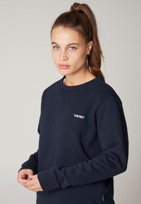 Felpa navy con scollatura a girocollo, maniche lunghe e un piccolo logo bianco "PROTEST" sul petto. Materiale in cotone morbido.