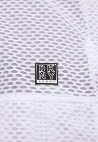 Weißer Netzstoff mit einem offenen Muster; verfügt über ein schwarzes Etikett mit "DKNY SPORT" in fetter Schrift am unteren Zentrum.