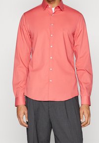 Coral long-sleeve button-up shirt with a spread collar, smooth texture, and silver buttons, paired with gray pinstriped trousers.