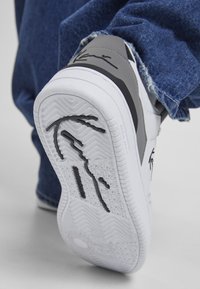 Baskets blanches avec des accents gris, arborant une semelle en caoutchouc texturé avec des motifs de relief distincts et un détail signature au talon.