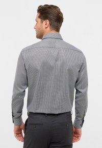 Camicia button-up con un motivo a scacchi bianco e nero. Presenta un colletto, maniche lunghe e dettagli a contrasto nei polsini.