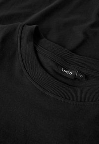 T-shirt in cotone nero con collo a coste e etichetta con il nome del marchio "LMTD", taglia 12-14, posizionata in piano per una chiara visibilità.