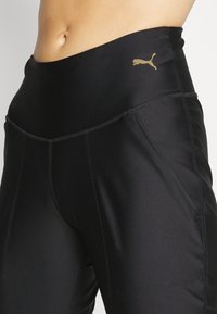 Czarne legginsy sportowe o gładkiej fakturze, z wysokim stanem i złotym logo Puma. Posiadają przeszywane szwy dla zwiększonej trwałości.