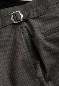 Dark gray pinstripe trousers featuring a metal buckle closure, waistband detailing, and discreet side pocket. Textured fabric with fine lines.