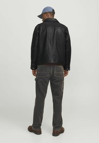 Black leather jacket with a collar, worn over dark gray pants. The outfit is complemented by a light blue cap and brown footwear.