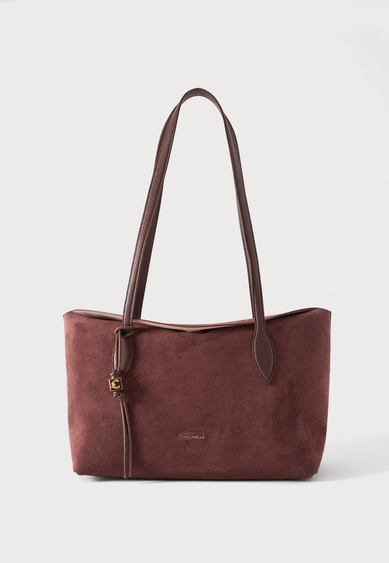 Sac cabas en daim marron avec longues bandoulières en cuir et pendentif logo doré, forme rectangulaire et nom de marque discret à l'avant.