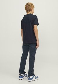 Camiseta de manga corta navy, pantalones oscuros y zapatillas azules con detalles en negro. Vista desde la parte posterior, mostrando un ajuste y diseño casual.