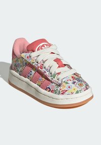 Barevná teniska s květinovým vzorem, bílým a růžovým textilním svrškem, bílými tkaničkami a podrážkou z gumy. Všimněte si texturovaných doplňků.