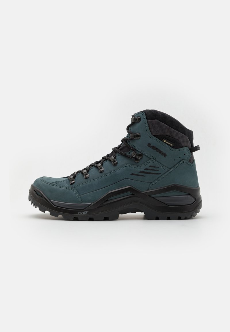 Scarpa da trekking di un verde scuro con tomaia in suede e sintetico, supporto alto alla caviglia e suola in gomma nera robusta. Presenta occhielli in metallo e cuciture.