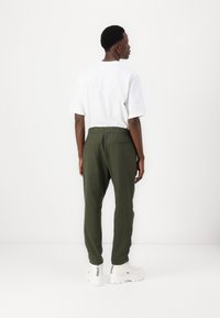 Olive green, lightweight joggers with elastic waistband and rear pocket, worn with a white t-shirt and white sneakers. Simple design.
