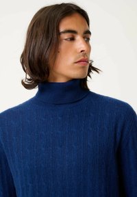 Dunkelblaues Rollkragenpullover aus strukturiertem Strickstoff, mit einem erhöhten Muster und einer taillierten Passform, die Wärme und Komfort betont.