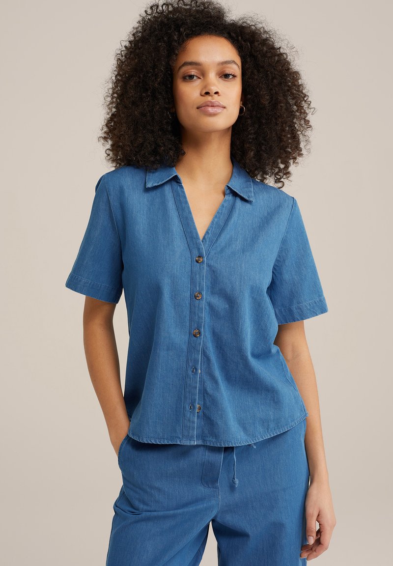 Zils džinsu krekls ar īsām piedurknēm, apkakli, pogu priekšpusi un brīvu piegriezumu. Tam ir nedaudz saplēsts apakšmalas un gluda tekstūra.