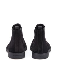 Černé semišové kotníkové boty s hladkou texturou, elastickými bočními panely a gumovou podrážkou. Obsahují minimální švy. Pohled zezadu.