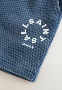 Sinine vakstikangas, millel on valged ümmargused tähed tekstiga "SAINT SALT LONDON".