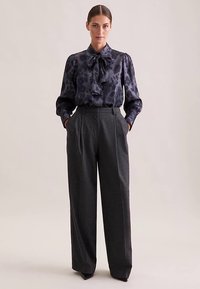 Dunkelblaue Bluse mit Leopardenmuster und Detail mit Schleife, kombiniert mit hochtaillierter, weit geschnittener grauer Hose. Glatter Stoff, maßgeschneiderte Passform.