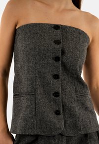 Top senza maniche a spina di pesce grigia con bottoni neri, caratterizzato da una forma aderente e tasche laterali. Tessuto testurizzato con un design sartoriale.