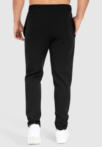 Zwarte sweatpants van zacht materiaal, met een relaxte pasvorm, een elastische tailleband en zijzakken. Gecombineerd met witte sportschoenen.
