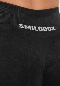 Czarne legginsy o dopasowanym kroju, z prążkowaną fakturą. Elastyczny pas jest ozdobiony nazwą marki "SMILODOX" w białym kolorze.