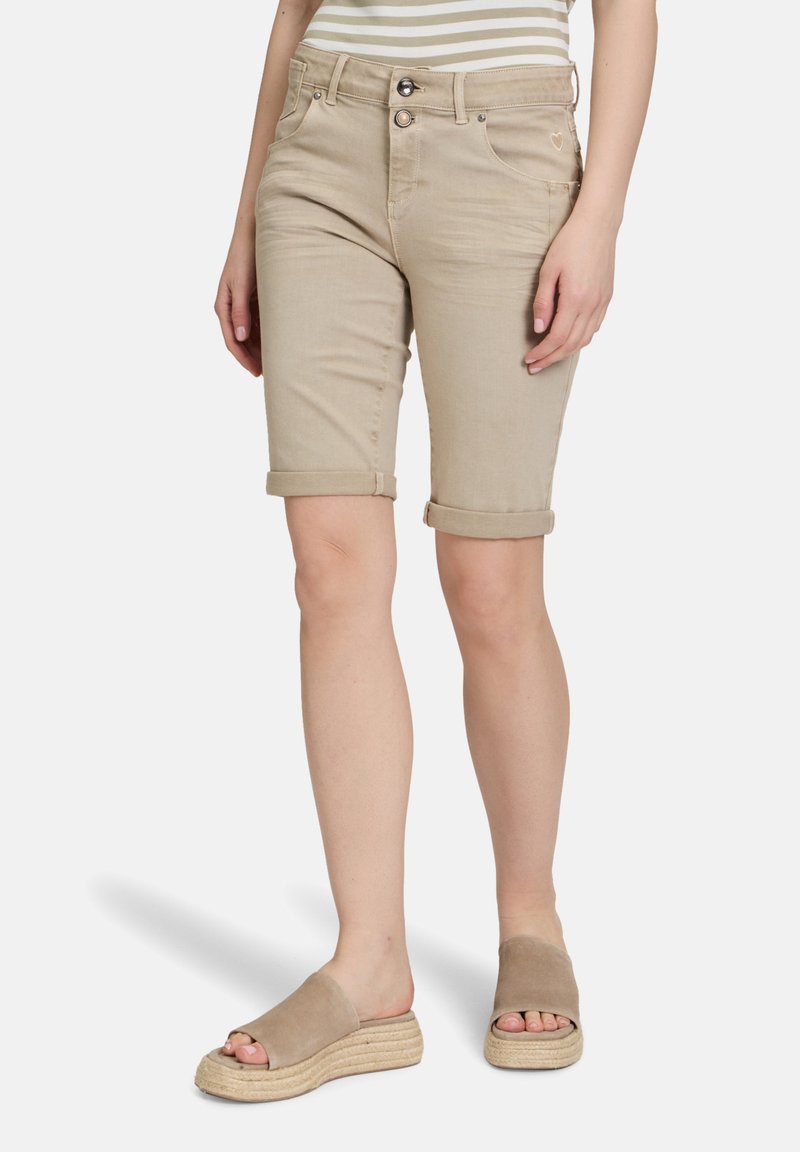 Shorts en denim beige avec ourlets retroussés, dotés d'une fermeture éclair et d'un bouton, de poches avant et d'un petit détail en forme de cœur sur le côté.