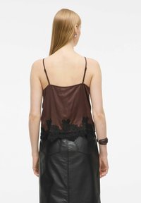 Brązowa satynowa koszulka na ramiączkach z cienkimi paskami i czarnym koronkowym wykończeniem, w połączeniu z czarną skórzaną spódnicą. Gładka tekstura i subtelny połysk.
