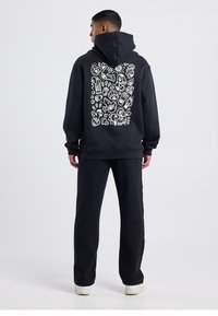 Black hoodie featuring a white graphic design on the back, paired with matching black joggers and white shoes. Soft material, relaxed fit.