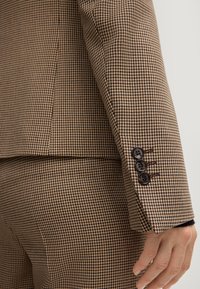 Giacca da abito marrone a motivo houndstooth con tessuto testurizzato, vestibilità slim e tre bottoni neri sui polsini.