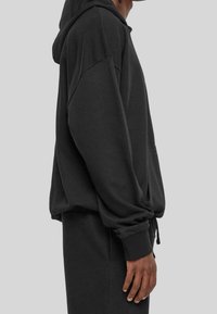 Sudadera negra hecha de un tejido suave, con un corte holgado, mangas largas, un bolsillo frontal y cordones en el dobladillo.