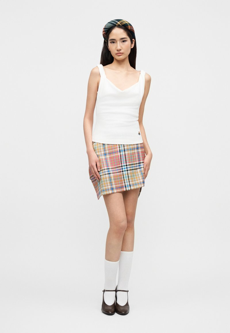 Weißes eng anliegendes Tanktop mit V-Ausschnitt, kombiniert mit einem mehrfarbigen karierten Minirock. Accessoires sind ein passendes kariertes Stirnband und weiße Socken.