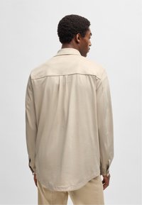 Beige langsl sleeve-shirt met een gladde textuur, met knoopmanchetten en een inzetstuk over de rug, ontworpen voor een ontspannen pasvorm.