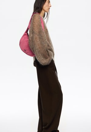 Różowa torebka na ramię wykonana z gładkiego materiału, o zaokrąglonym kształcie i zamknięciu na zamek. Niesiona z przytulnym, oversized brązowym swetrem i brązowymi spodniami.