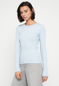 Svetlo modra oprijeta majica z dolgimi rokavi iz rebraste tkanine z okroglim izrezom in brezkrajnišči, kombinirana z sivimi hlačami širokih nog.