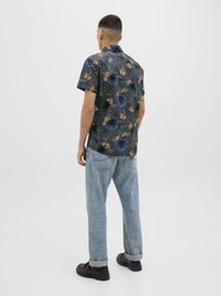 Chemise à manches courtes en tissu sombre avec des motifs floraux et de feuilles colorés, assortie à un jean en denim clair et des chaussures marron.