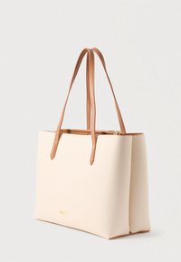 Sac fourre-tout en crème avec un simili cuir lisse, des poignées contrastantes en tan, une forme rectangulaire et un accent logo doré sur le devant.