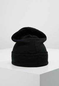 Fekete kötött sapka dupla rétegű hajtással, puha tapintással és kerek felső résszel. A dizájn jellemzője a hátoldalon található varrás nélküli csatlakozás.