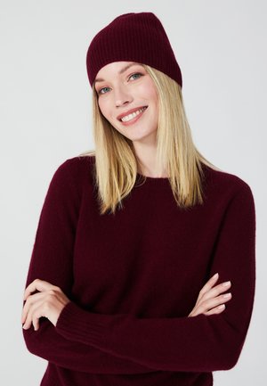 Beanie a maglione in maglia color bordeaux con texture a coste, abbinato a un comodo maglione coordinato. Il maglione presenta un collo rotondo e maniche lunghe.
