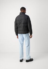 Svart pufferjakke med høy krage, quiltet design og glatt tekstur. Kombinert med lyseblå jeans og svarte støvler.