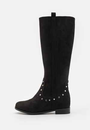 Botte noire montant jusqu'au genou avec un petit talon et des détails cloutés argentés autour de la cheville, en matière imitation daim.
