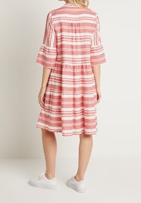Bunt gekleidetes Kleid mit schichtweise angeordneter Rockpartie, das rote und weiße horizontale Streifen aufweist und einen lockeren Schnitt hat. Getragen mit weißen Sneakers.