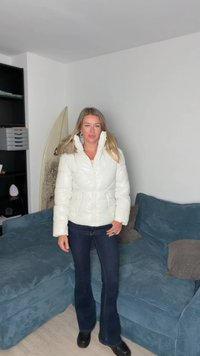 Giacca imbottita bianca con collo alto, design trapuntato, chiusura frontale con zip e due tasche laterali. Abbinata a jeans scuri a zampa d'elefante e stivali neri.