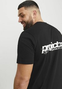 Camiseta de algodón negra con una impresión gráfica blanca en la parte posterior, que muestra el texto "project." en una fuente moderna y en negrita.