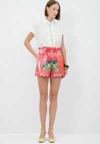 Blusa blanca de manga corta con detalle de botones, combinada con pantalones cortos de cintura alta de patrón floral multicolor. Zapatos cerrados amarillos.
