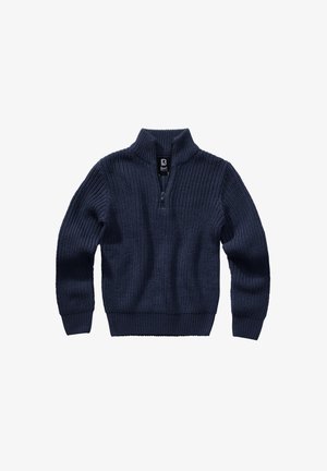 Person iført en mørkstrikket sweater med ærmer, der dækker håndleddene, hænder presset sammen i en bøn eller hilsen gestus.
