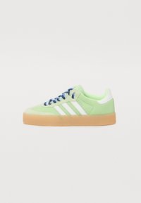 Låg sneaker i pastellgrönt med vita ränder, blå och vita skosnören samt en tjock gummisula, visad från sidan mot en vit bakgrund.