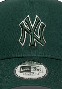 Zielona czapka bejsbolowa z białym i ciemnozielonym haftowanym logo "NY". Posiada markowy regulowany zapięcie typu snapback z okrągłą metką.