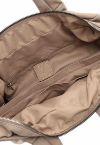 Intérieur d'un sac en tissu beige avec une poche zippée, doublure douce, et une petite étiquette en cuir avec la marque. Ouverture zippée en haut.