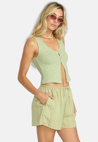 Svijetlozeleni rebrasti crop top s dugmadi, uparen sa svijetložutim prugastim šortsevima s elastičnim pojasom i džepovima.